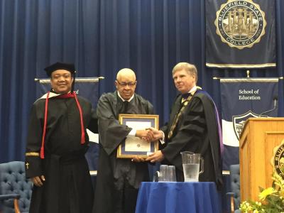 At Bluefield State College’s 2019 Commencement, BSC President Robin Capehart (right) announced that the College Library has been renamed in honor of BSC alumnus William B. Robertson (center).  The Bluefield State College Board of Governors, whose chairman, the Reverend Garry D. Moore is pictured (left) with Mr. Robertson and President Capehart, voted unanimously to rename the library to honor Mr. Robertson.
